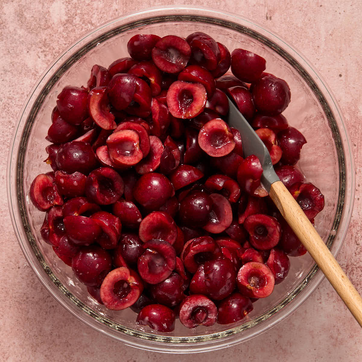 Halved cherries tossed with cornstarch in a large glass bowl.