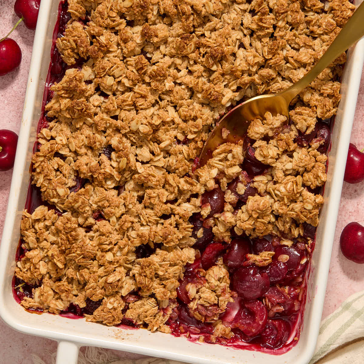 Gluten-free cherry crisp in a white baking dish with a serving spoon scooping some out.