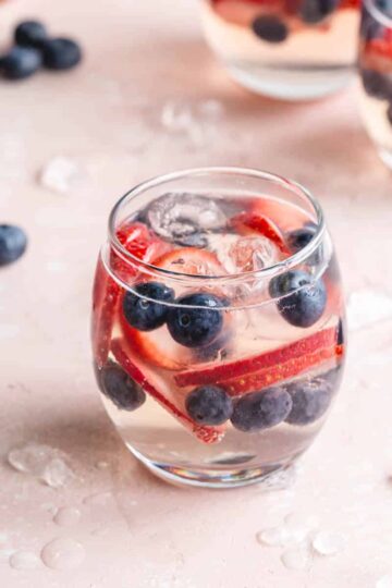 White wine spritzer served in a stemless wine glass with strawberry slices and blueberries.