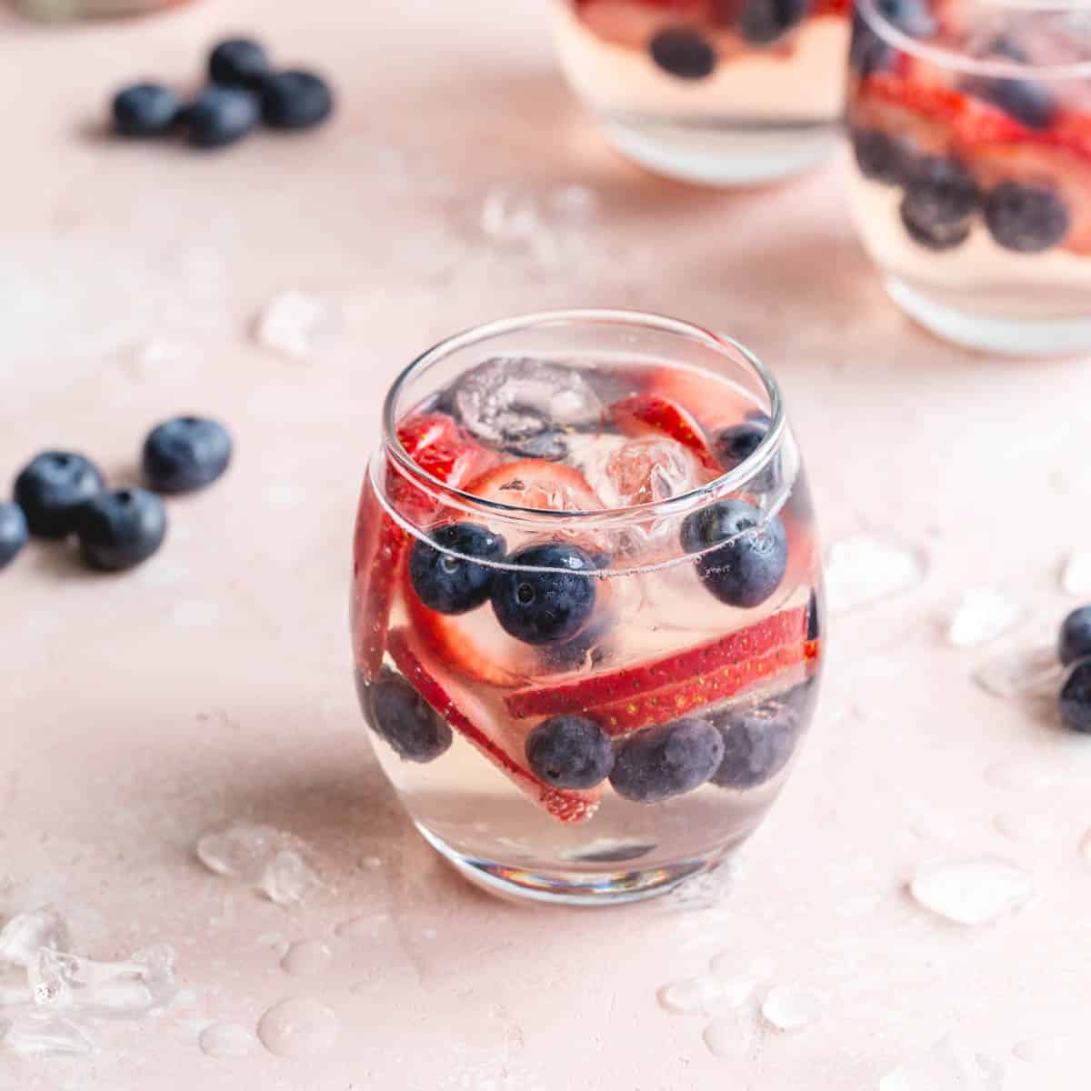 White wine spritzer served in a stemless wine glass with strawberry slices and blueberries.