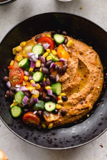 Overhead of black bean hummus served in a black bowl with veggie toppings.