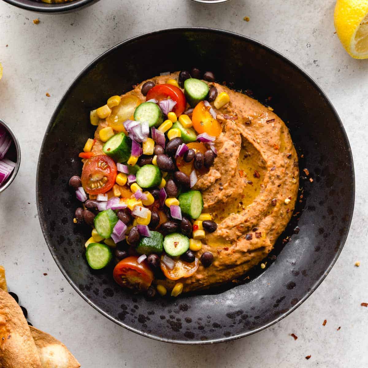 Overhead of black bean hummus served in a black bowl with veggie toppings.