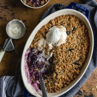 Healthy blueberry crisp baked up in a blue dish and topped with ice cream.