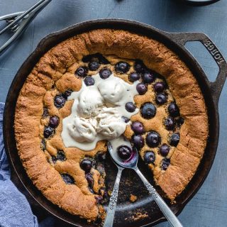 Overhead view of a blueberry skillet cookie topped with ice cream and two spoons inserted into it.