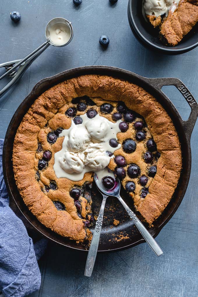 Overhead view of a blueberry skillet cookie topped with ice cream and a piece missing.