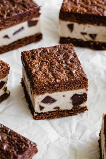 Brownie ice cream sandwiches cut into squares and arranged on white parchment paper.
