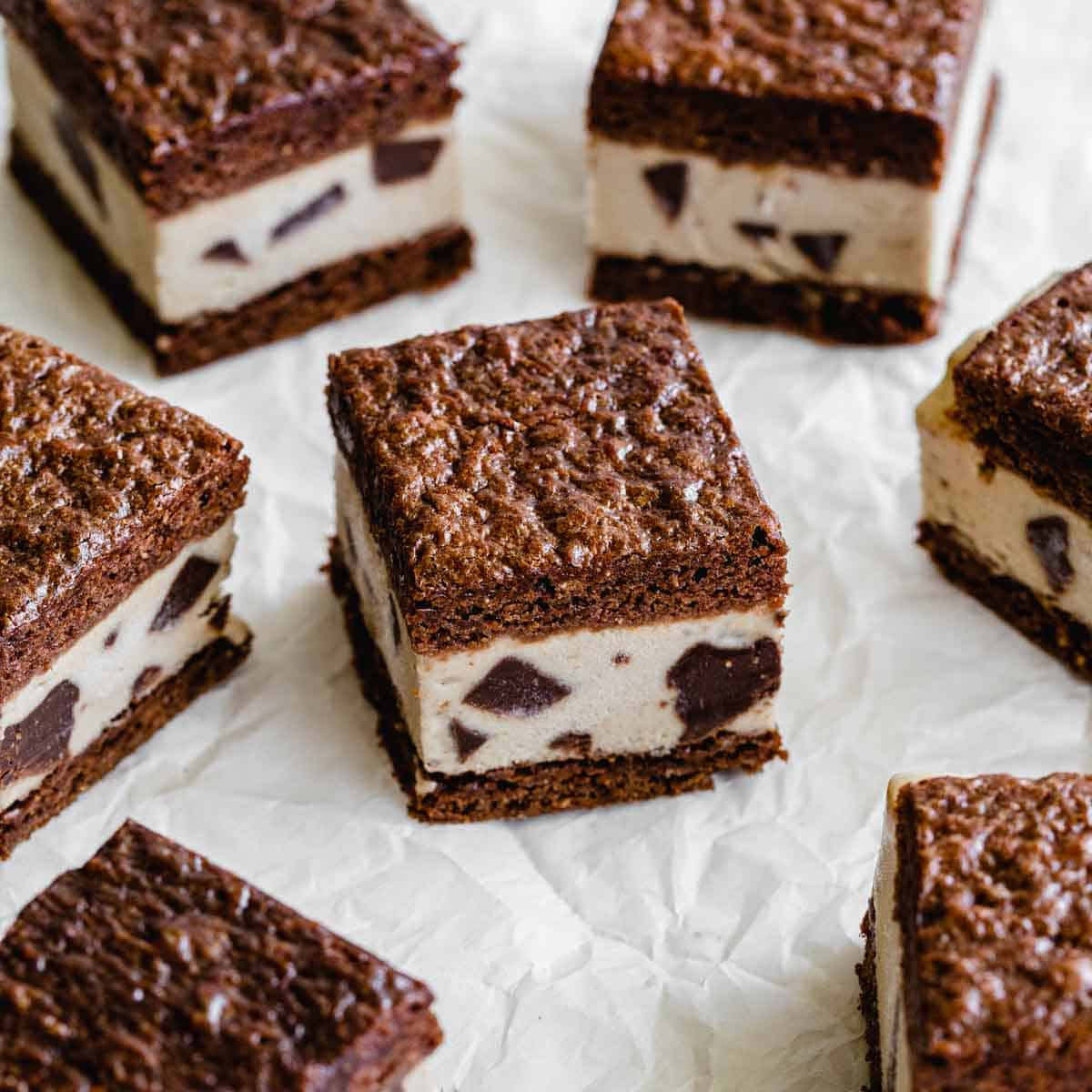 Brownie ice cream sandwiches cut into squares and arranged on white parchment paper.
