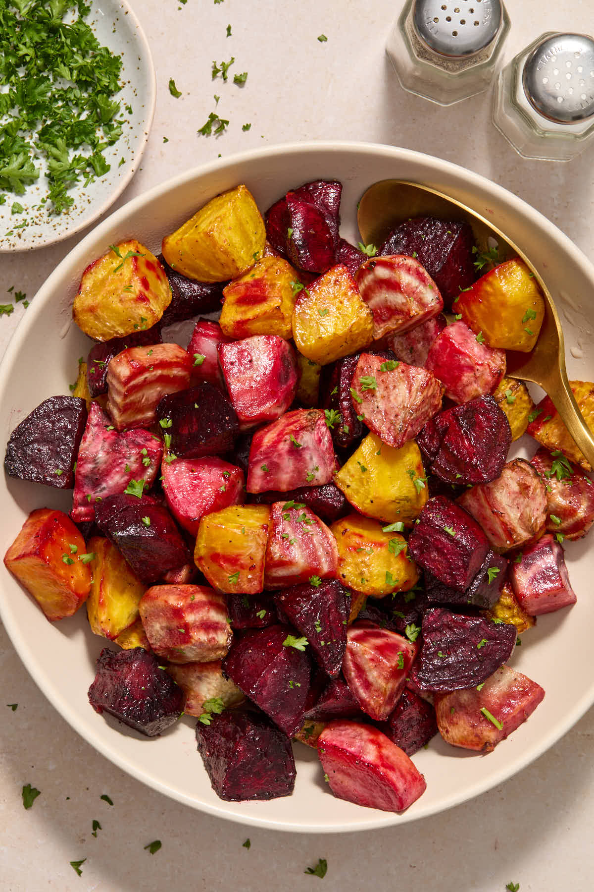 Beets served in a white bowl with salt and pepper and chopped parsley on the side.