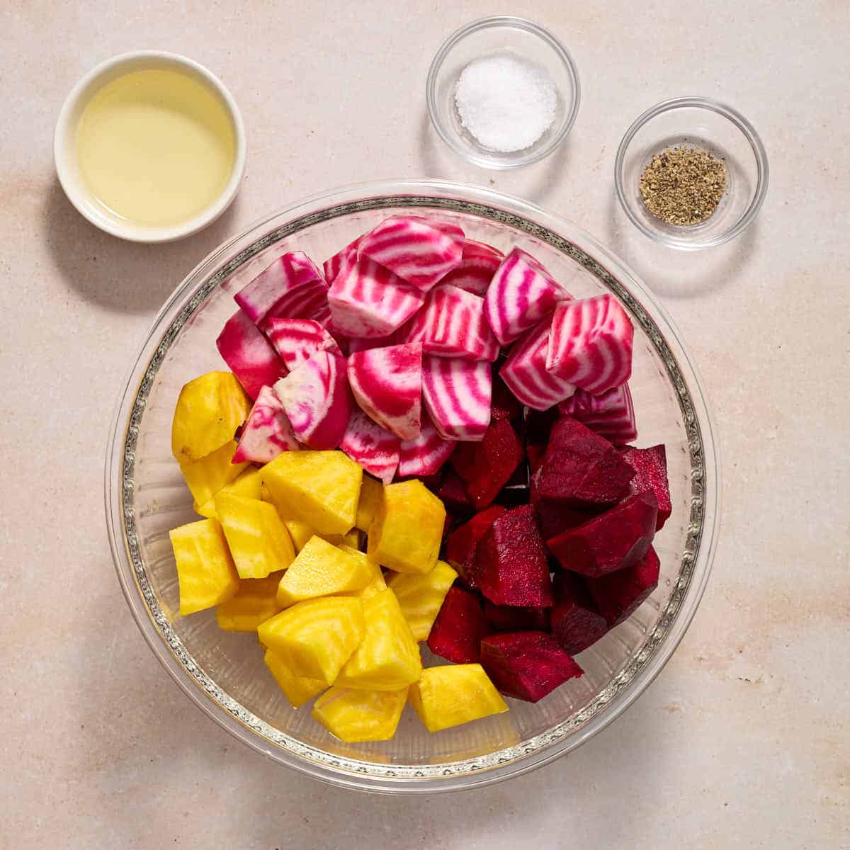 Chopped beets in a glass bowl with oil, salt and pepper on the side.