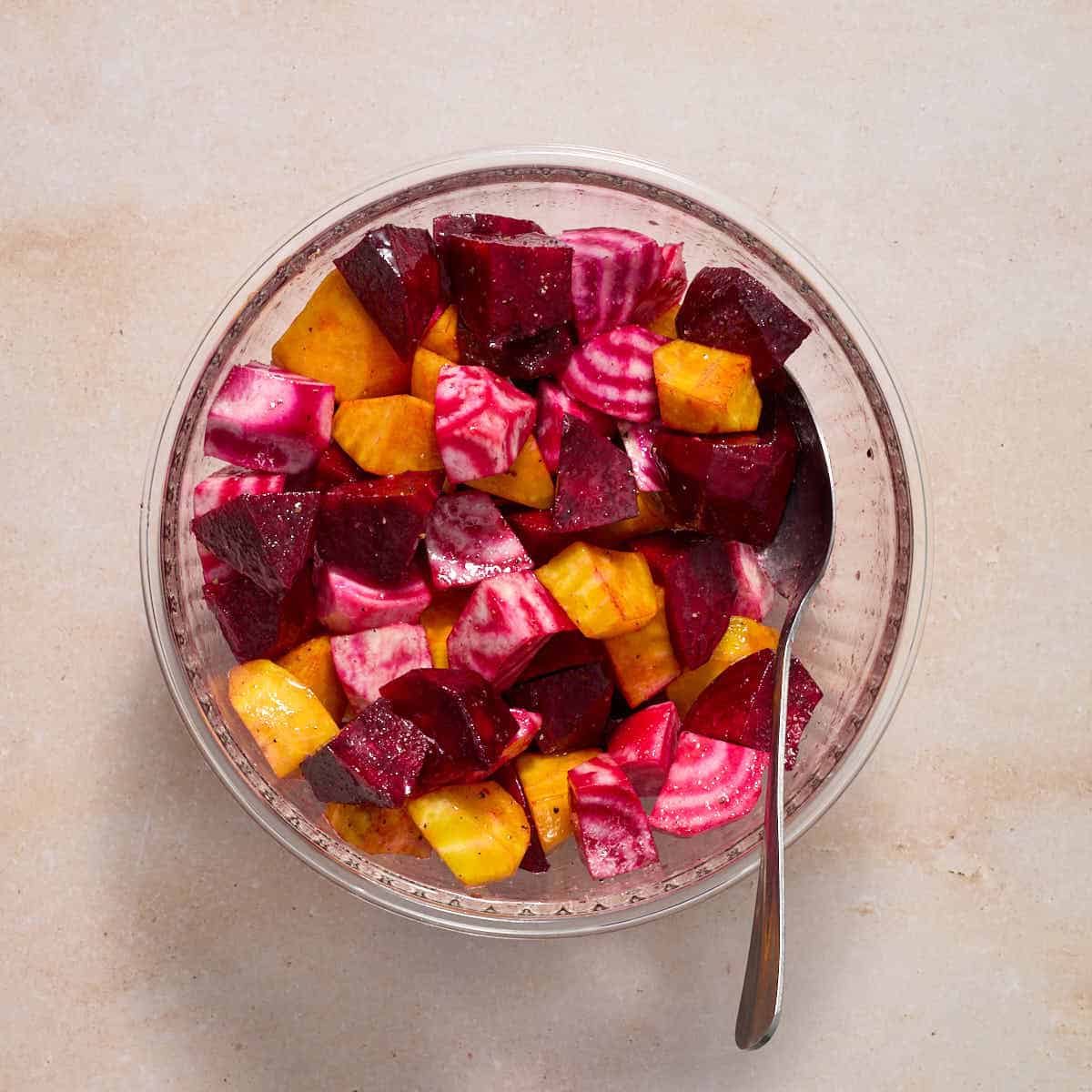 Chopped beets tossed with oil, salt and pepper in a glass bowl with a spoon.