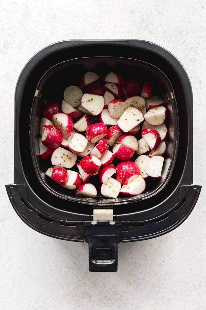 Overhead view of raw and seasoned radishes in the air fryer basket.