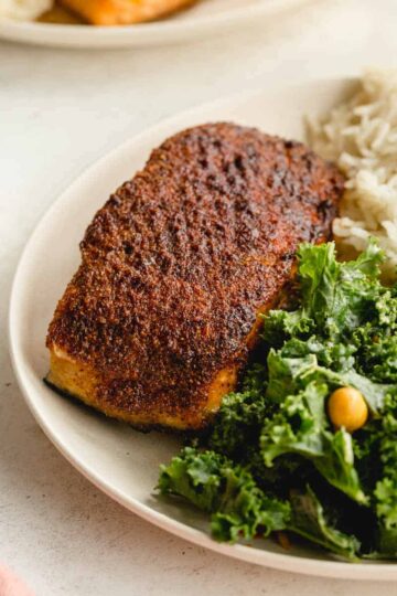 Angled view of an air fried salmon fillet on a plate with greens and rice.