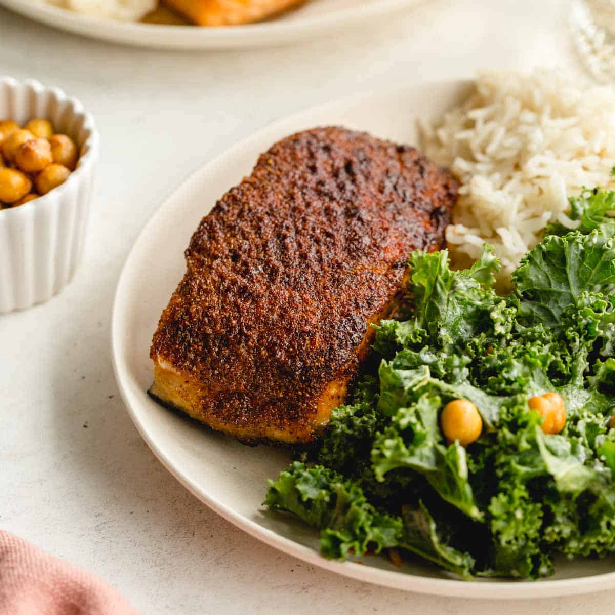 Angled view of an air fried salmon fillet on a plate with greens and rice.