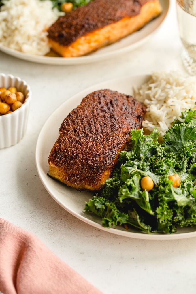 Up close view of crispy air fryer salmon on a plate with a kale and rice, with another plate of the same in the background.