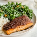 Up close view of a piece of air fryer salmon plated with a green salad and rice.