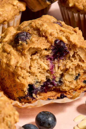 A blueberry oatmeal muffin on a muffin wrapper with a bite removed.