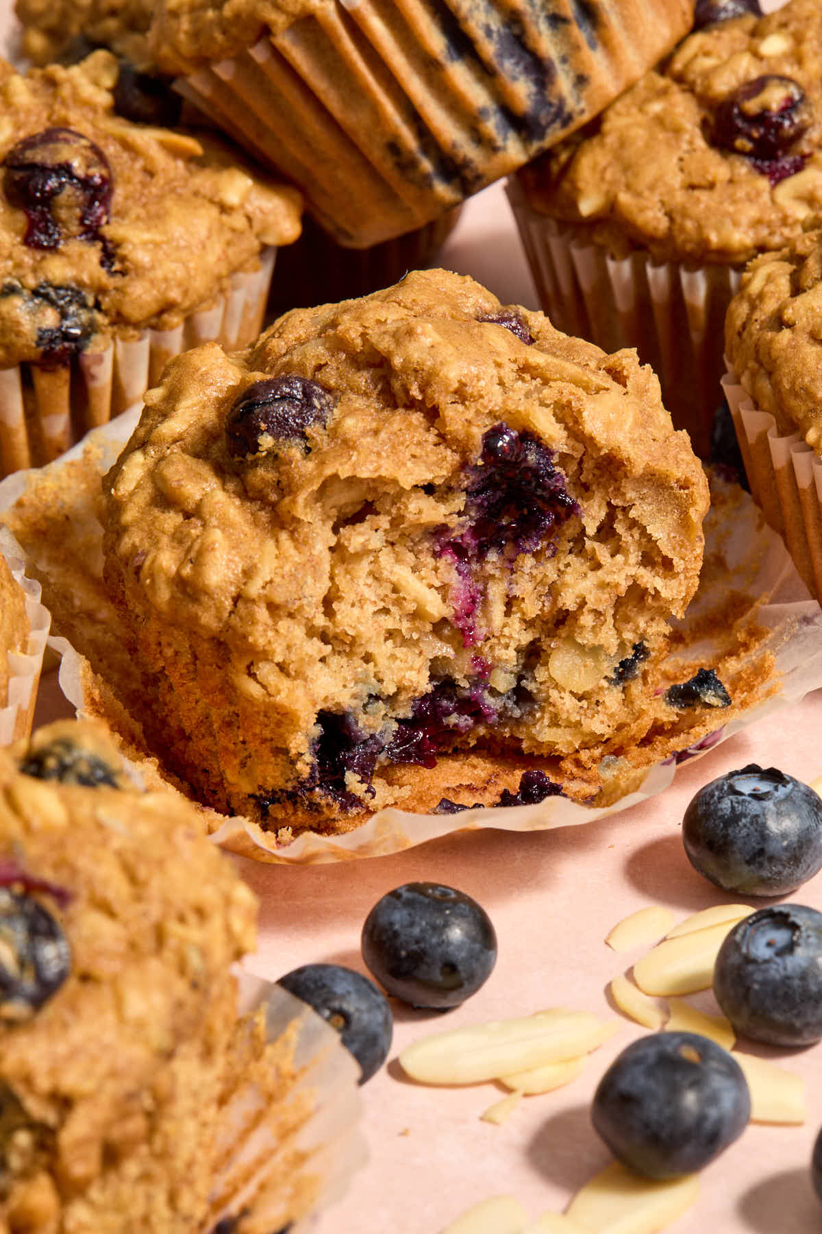 Muffin with bite removed on a muffin wrapper with other muffins around it.