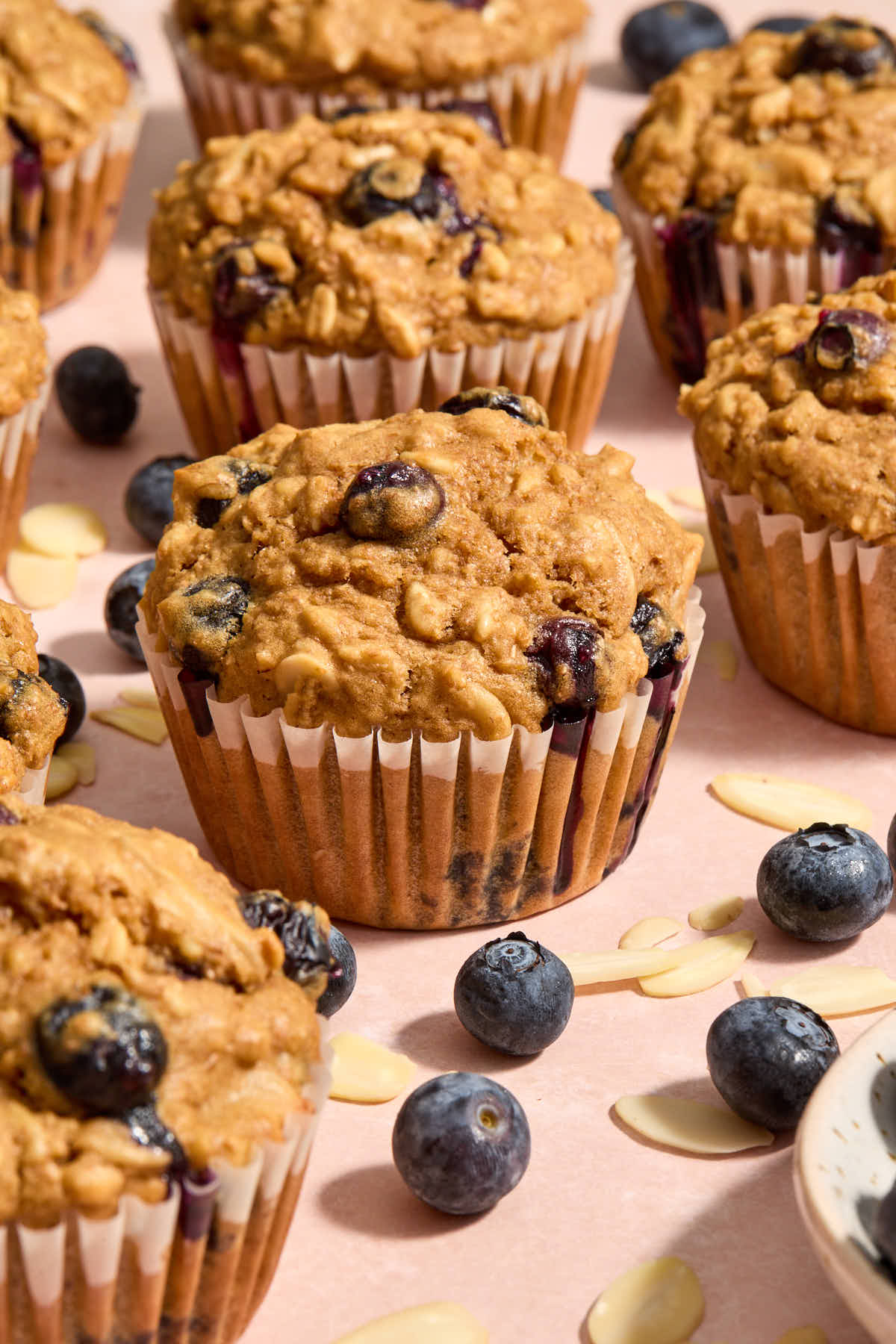 Blueberry muffin on a pink surface with other muffins, blueberries and almonds around it.