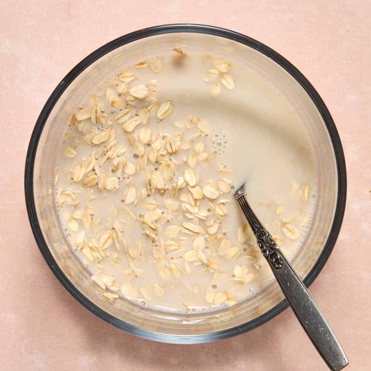 Oats and oat milk stirred together in a bowl with a spoon.