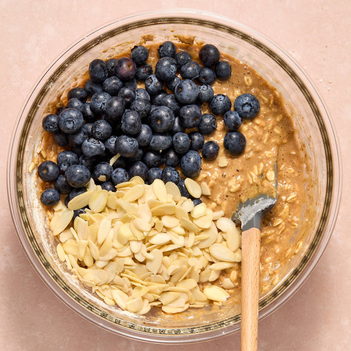 Muffin batter in a glass bowl with blueberries and almond slices on top.