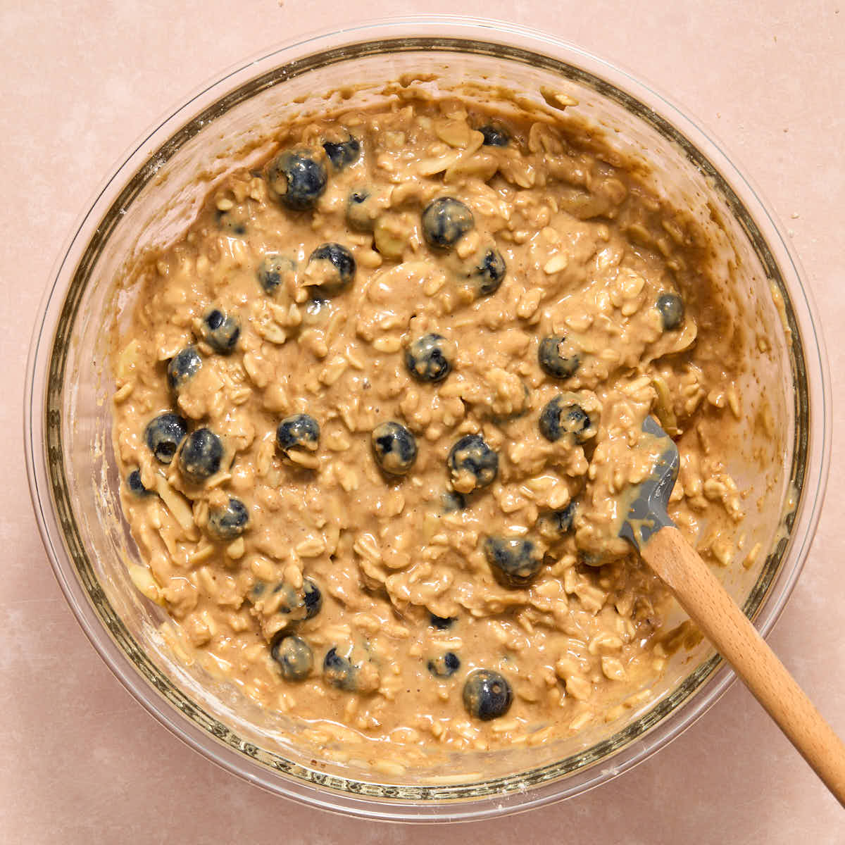 Muffin batter with blueberries and almonds stirred in with a spatula.