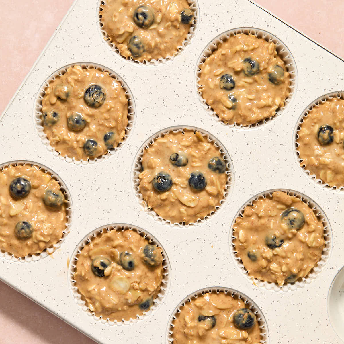 Muffin batter divided into 9 cavities in a white muffin pan.