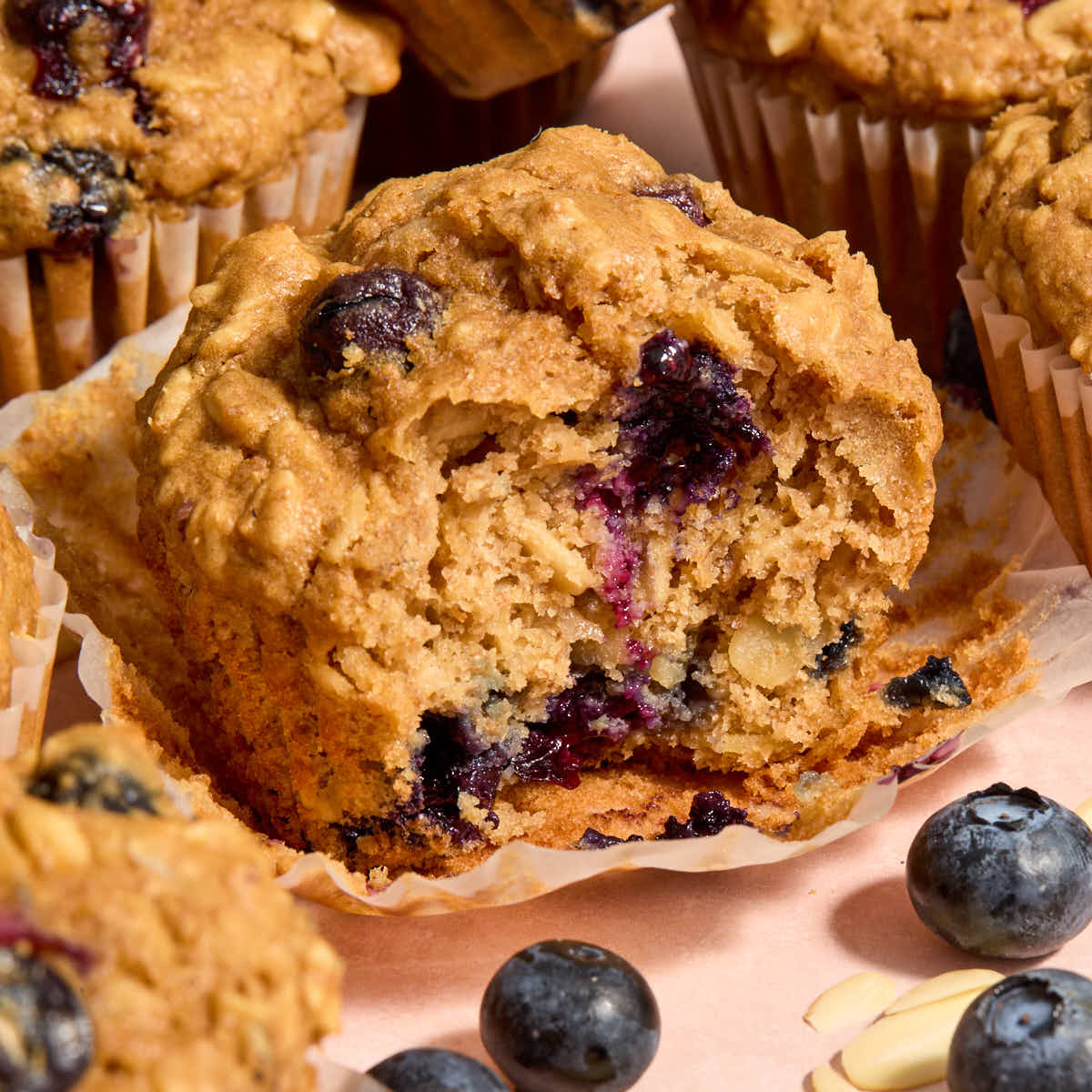 A blueberry oatmeal muffin on a muffin wrapper with a bite removed.