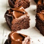 Angled view of square pieces of double chocolate zucchini cake on white parchment paper.