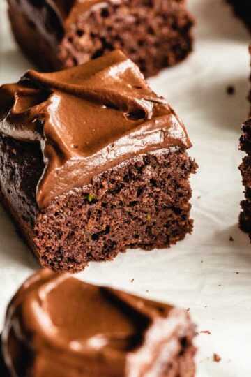 Angled view of square pieces of double chocolate zucchini cake on white parchment paper.