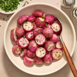 Air fryer radishes served in a white bowl with a spoon and chopped parsley on the side.