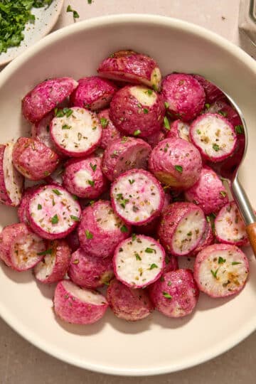 Air fryer radishes served in a white bowl with a spoon and chopped parsley on the side.
