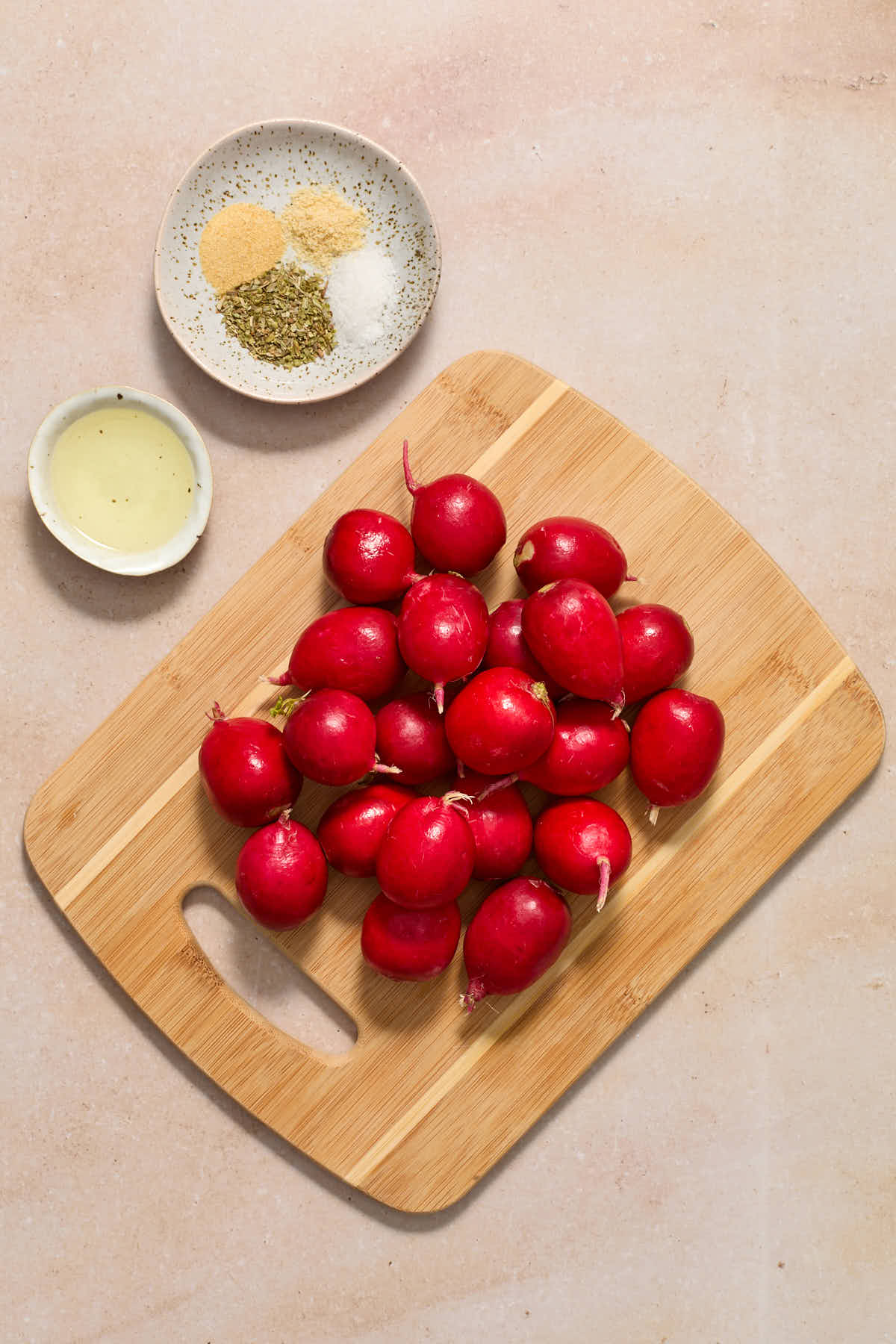 Radishes on a wooden board with oil and seasonings on the side.