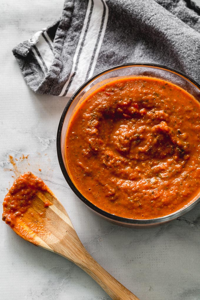 Overhead view of marinara sauce in a glass bowl with a wooden spoon and napkin off to the side.