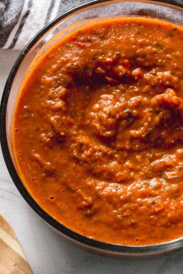 Overhead of fresh marinara sauce in a glass bowl with a wooden spatula on the side.