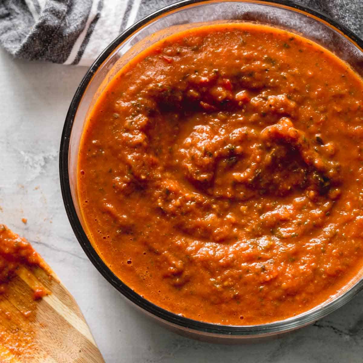 Overhead of fresh marinara sauce in a glass bowl with a wooden spatula on the side.