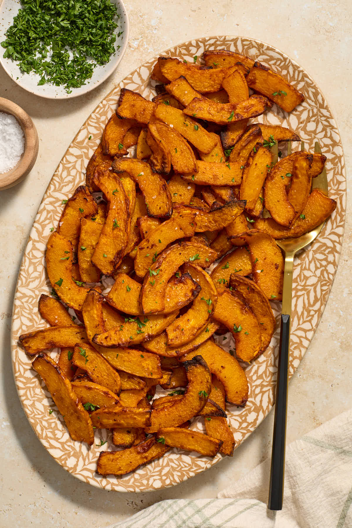 Pumpkin fries served on a platter with a serving fork and salt and parsley on the side.