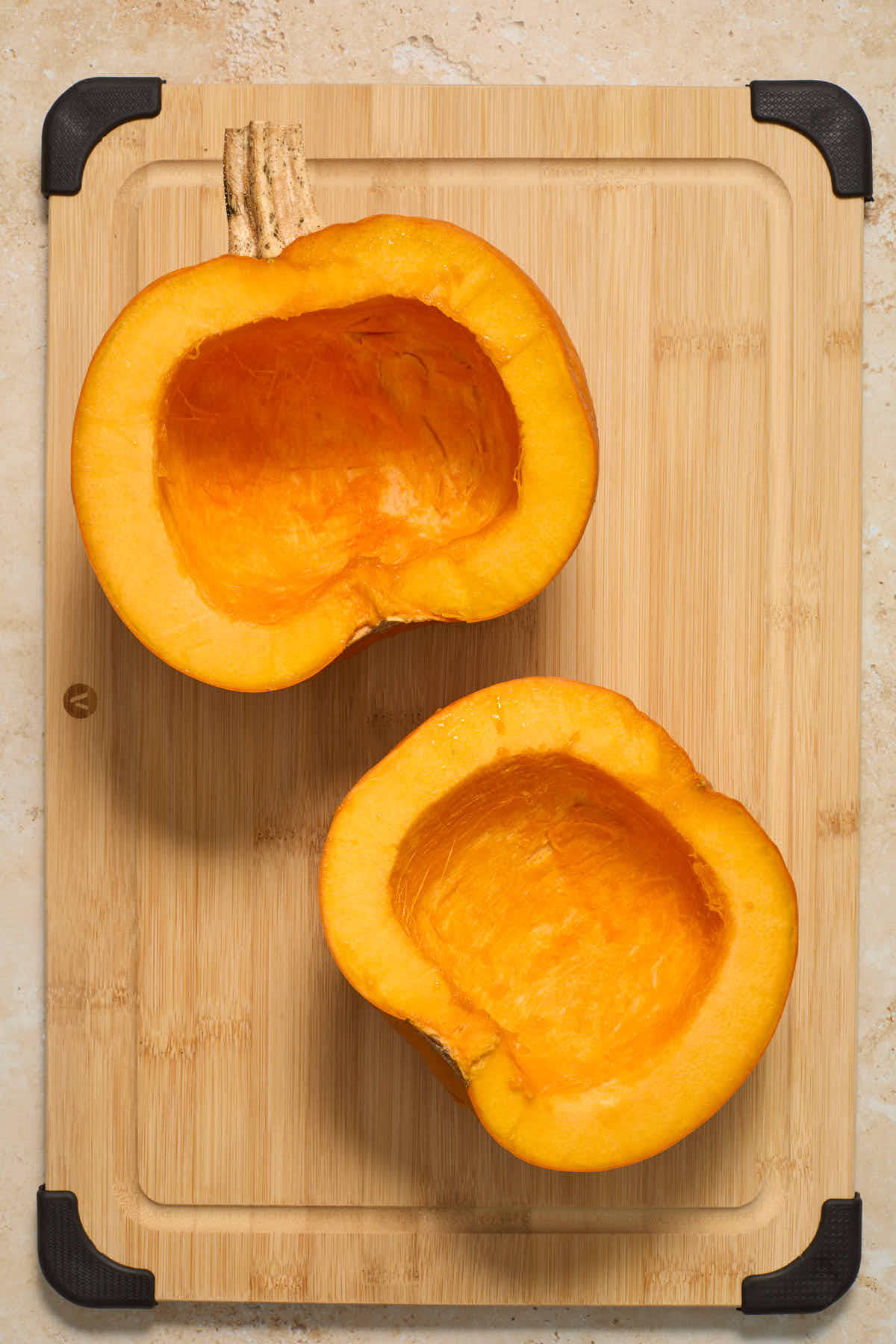 Two pumpkin halves on a wooden board with the seeds scooped out.