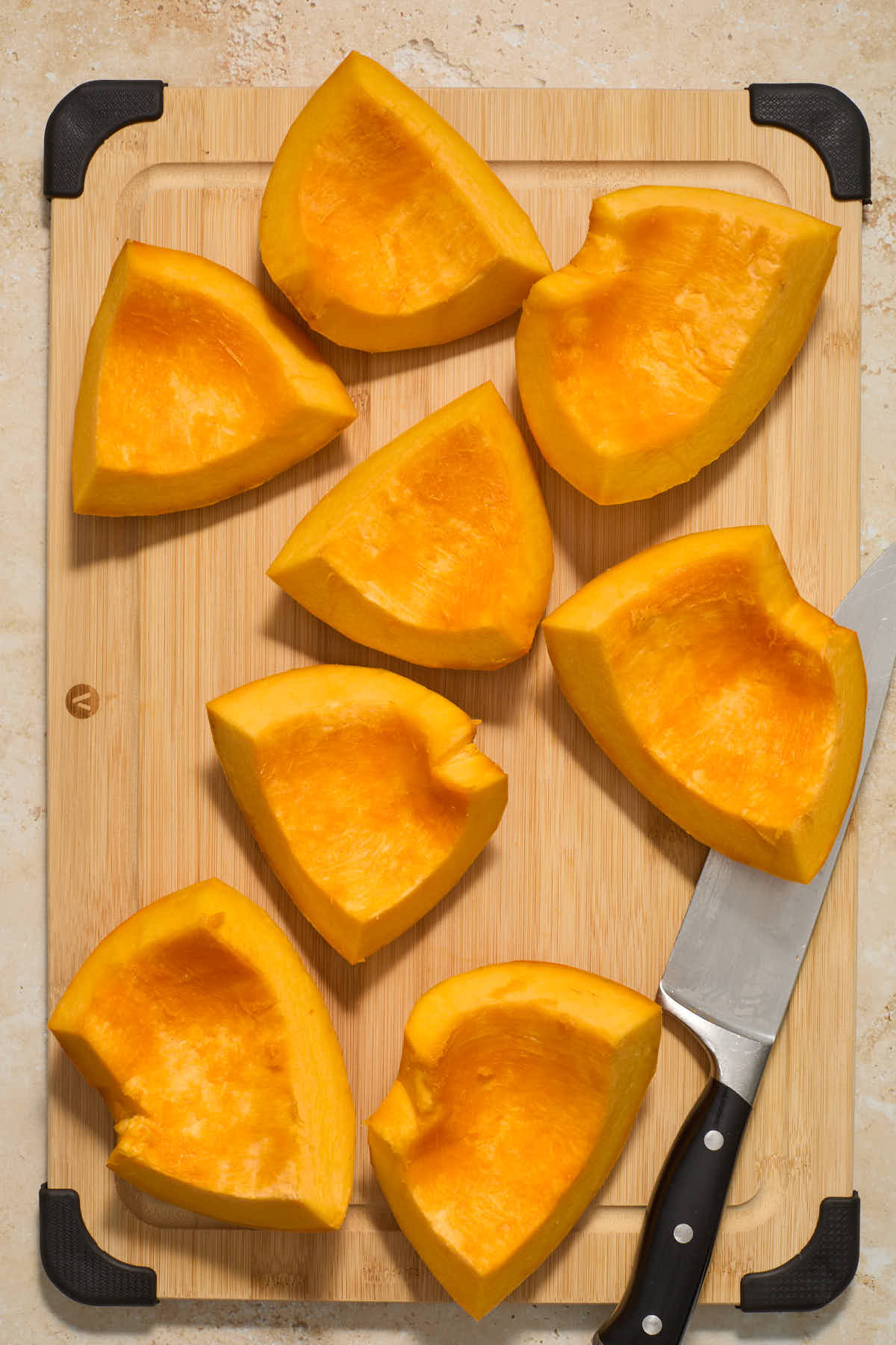 Pumpkin cut into 8 smaller pieces and arranged on a wooden board with a knife on the side.