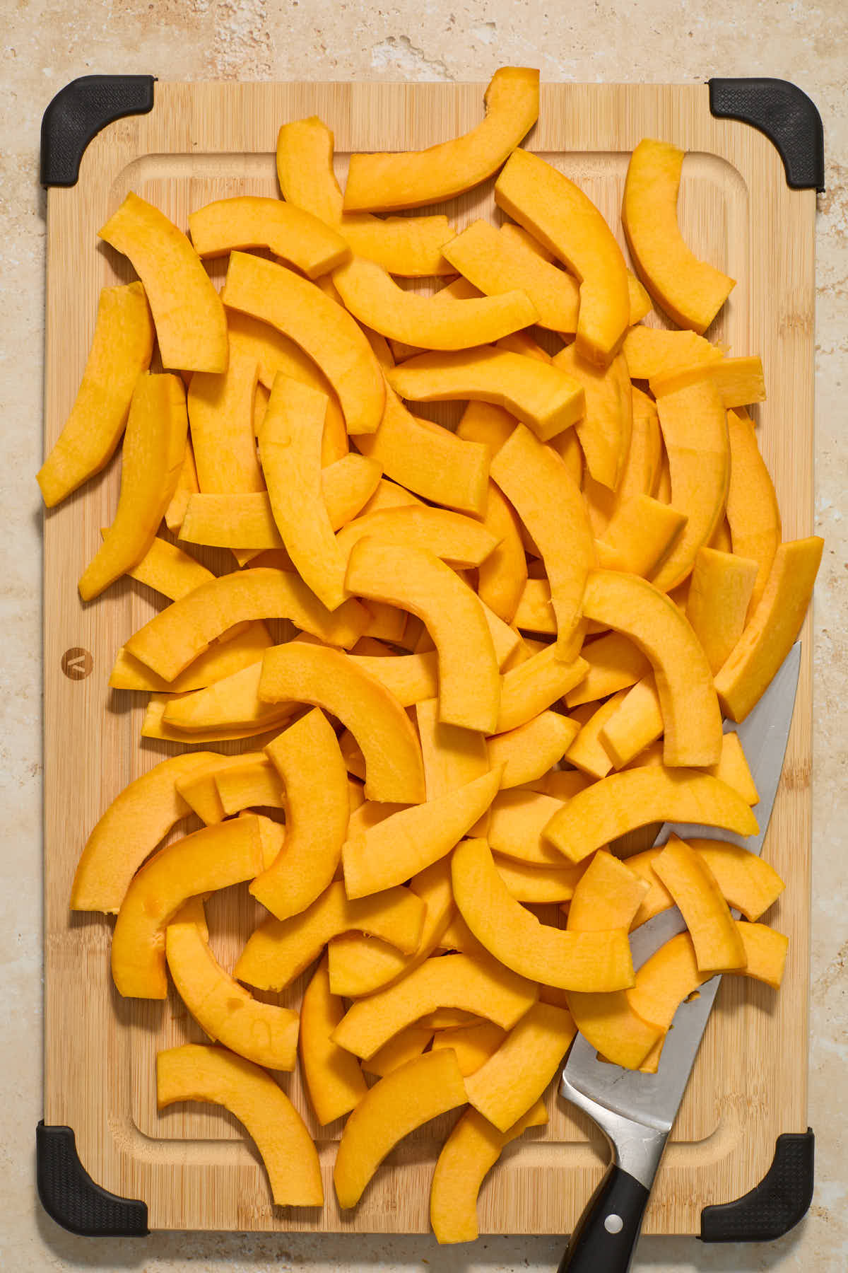 Pumpkin slices spread out on a wooden board with a knife on the side.