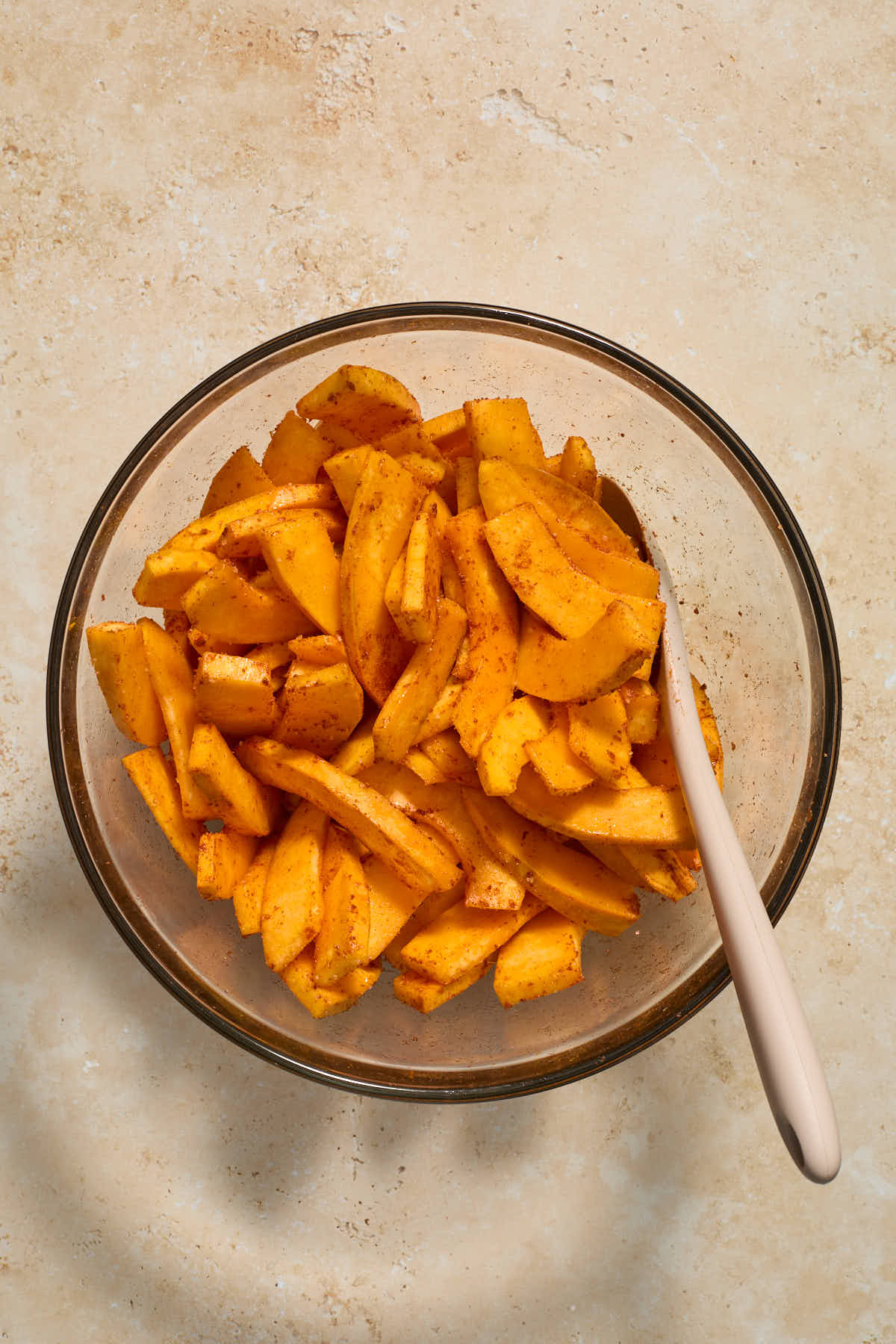 Pumpkin slices coated in oil and seasonings in a bowl with a spatula.