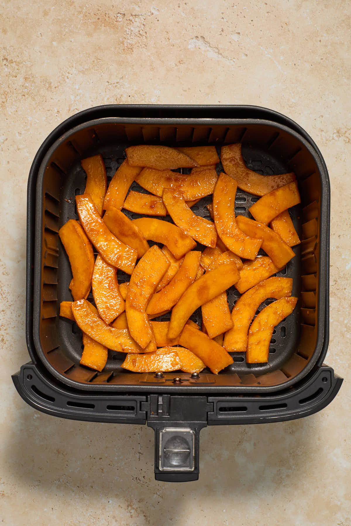 Seasoned pumpkin slices arranged in the air fryer basket.