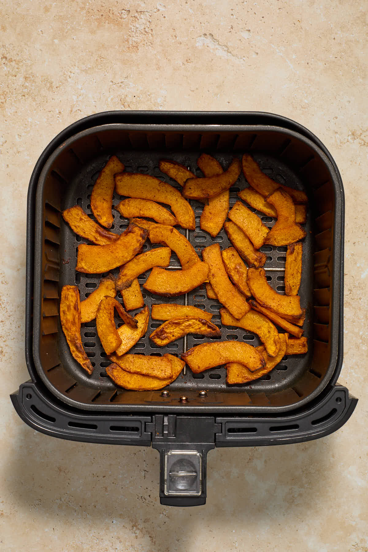 Air fried pumpkin slices in the air fryer basket.