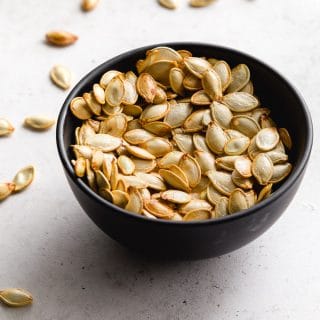 Air fryer pumpkin seeds in a small black bowl with seeds scattered around it.