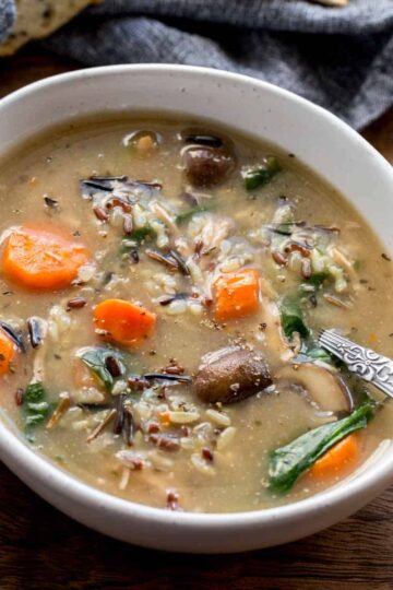Chicken and wild rice soup in a white bowl with a spoon inserted into it.