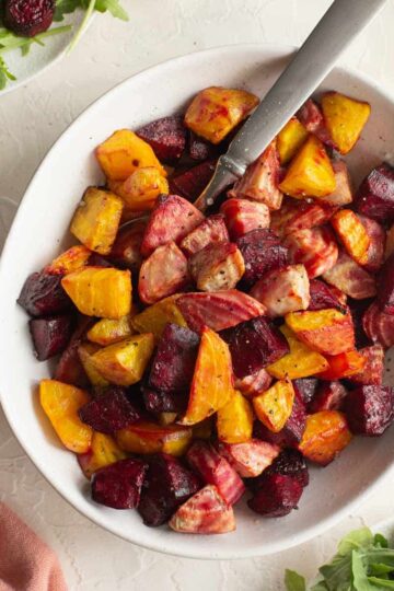 Chopped beets (red, golden and candy cane) air fried and served in a white bowl with a spoon.