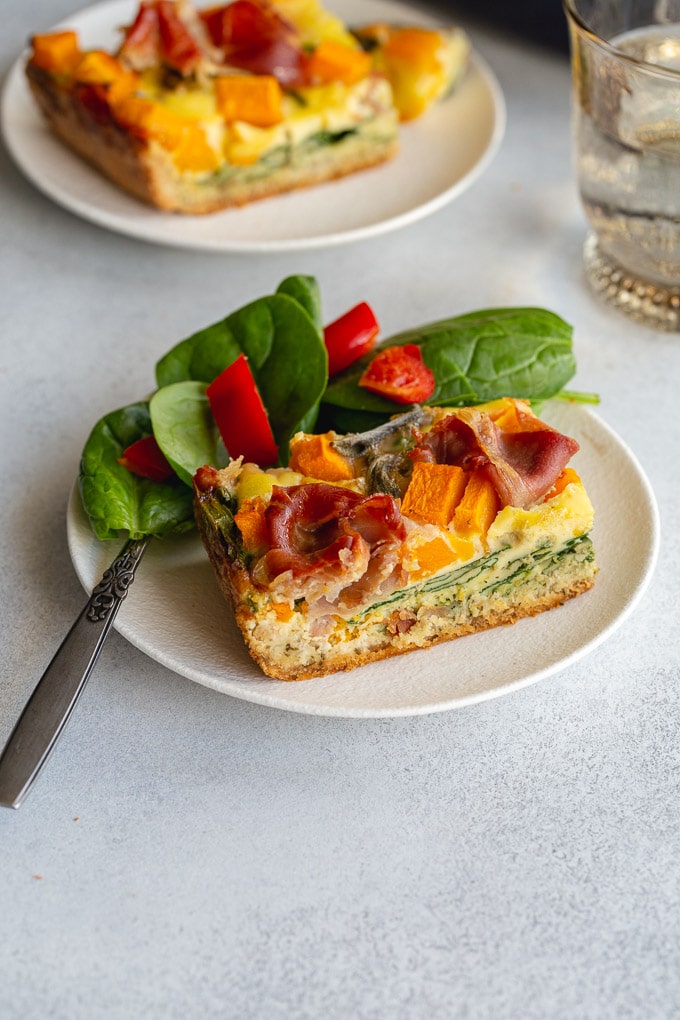 Side view of a slice of quiche on a white plate with a salad.