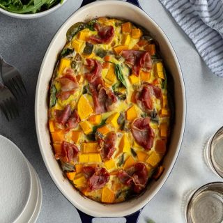 Overhead view of butternut squash quiche in an oval baking dish with a bowl of salad on the side.