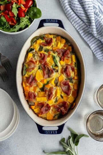 Overhead view of butternut squash quiche in an oval baking dish with a bowl of salad on the side.
