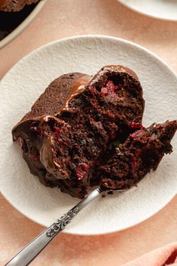 Slice of chocolate cranberry cake on a white plate with a fork.