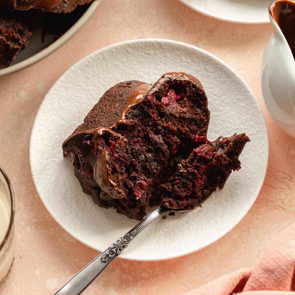 Slice of chocolate cranberry cake on a white plate with a fork.